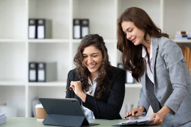Cheerful young female entrepreneur browsing tablet and laptop at workplace in office.